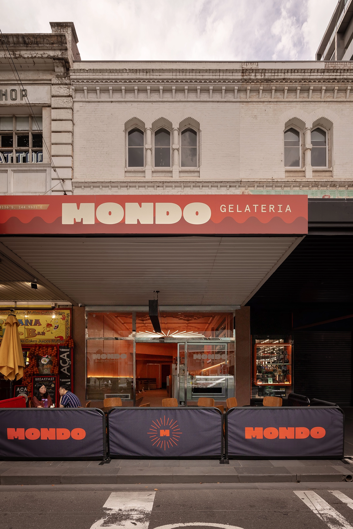 Exterior view of Mondo Gelateria's heritage storefront on Elizabeth Street, Melbourne, with red branding and outdoor seating.