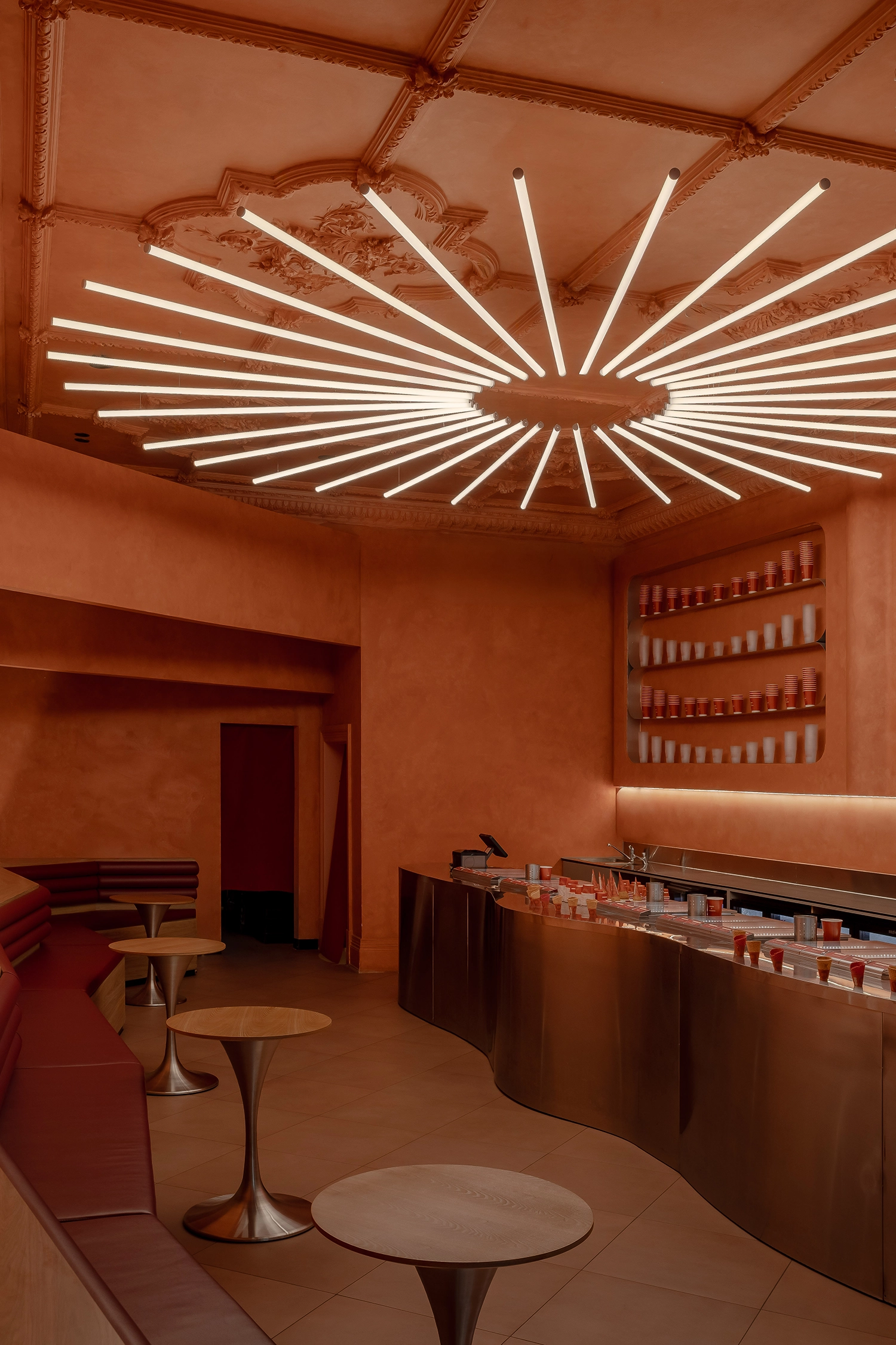 Interior view of the curved stainless steel counter and the radial sun-burst light fixture hanging from an ornate ceiling.
