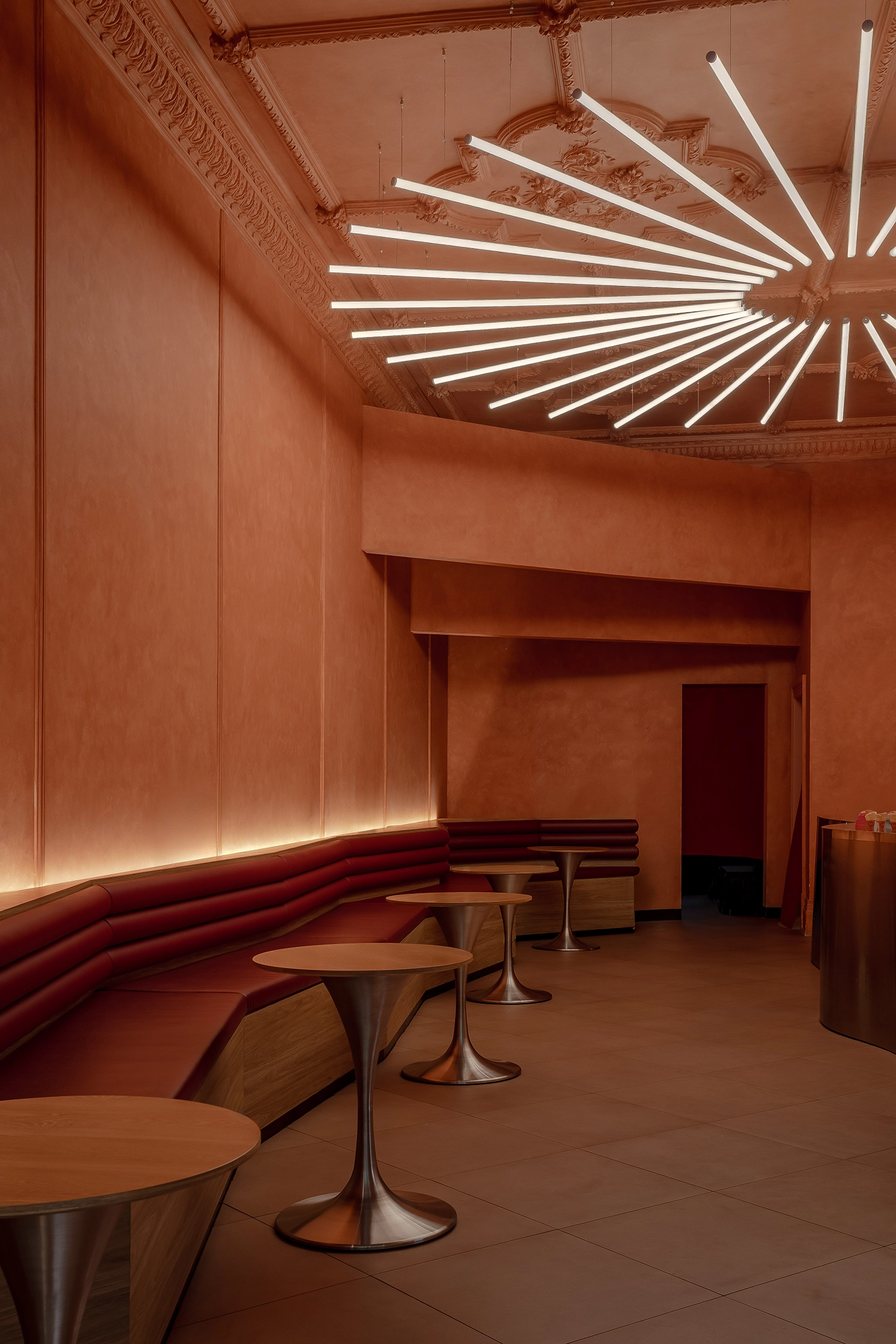 View of the seating area featuring deep burgundy leather banquettes and minimalist tulip-style wooden tables.