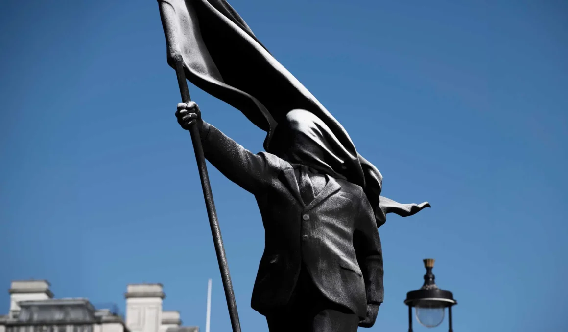 Close-up of Banksy's Anonymous Flag-Bearer bronze sculpture showing a faceless figure in a suit holding a flag.