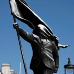 Close-up of Banksy's Anonymous Flag-Bearer bronze sculpture showing a faceless figure in a suit holding a flag.