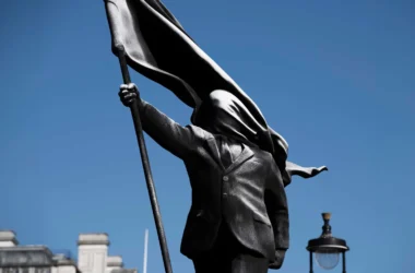 Close-up of Banksy's Anonymous Flag-Bearer bronze sculpture showing a faceless figure in a suit holding a flag.