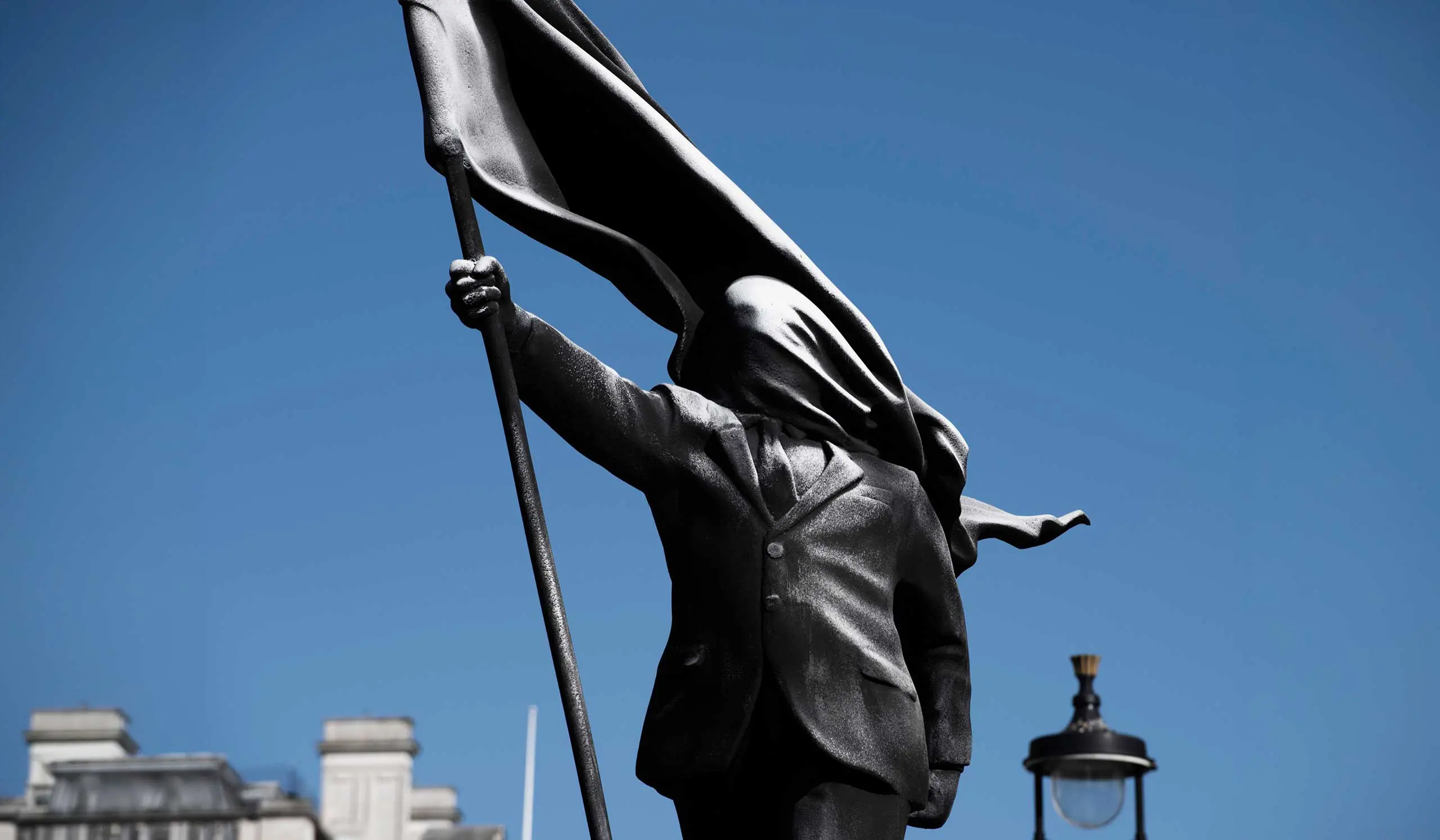 Close-up of Banksy's Anonymous Flag-Bearer bronze sculpture showing a faceless figure in a suit holding a flag.