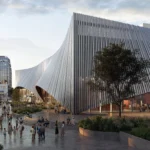 Pedestrians walking along a stone plaza next to a modern building with a sweeping, metallic ribbed facade in Nashville.