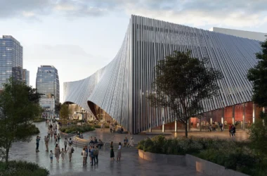 Pedestrians walking along a stone plaza next to a modern building with a sweeping, metallic ribbed facade in Nashville.