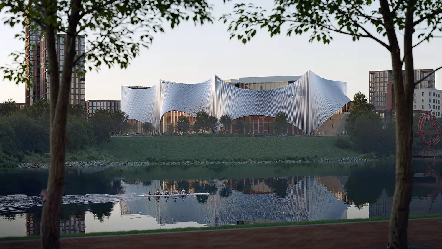 View across a calm river reflecting a large, silver building with arched openings and a rowing crew in the water.