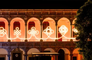 Illuminated LED knots by BIG and Artemide glowing against the Renaissance arches of the University of Milan at night.