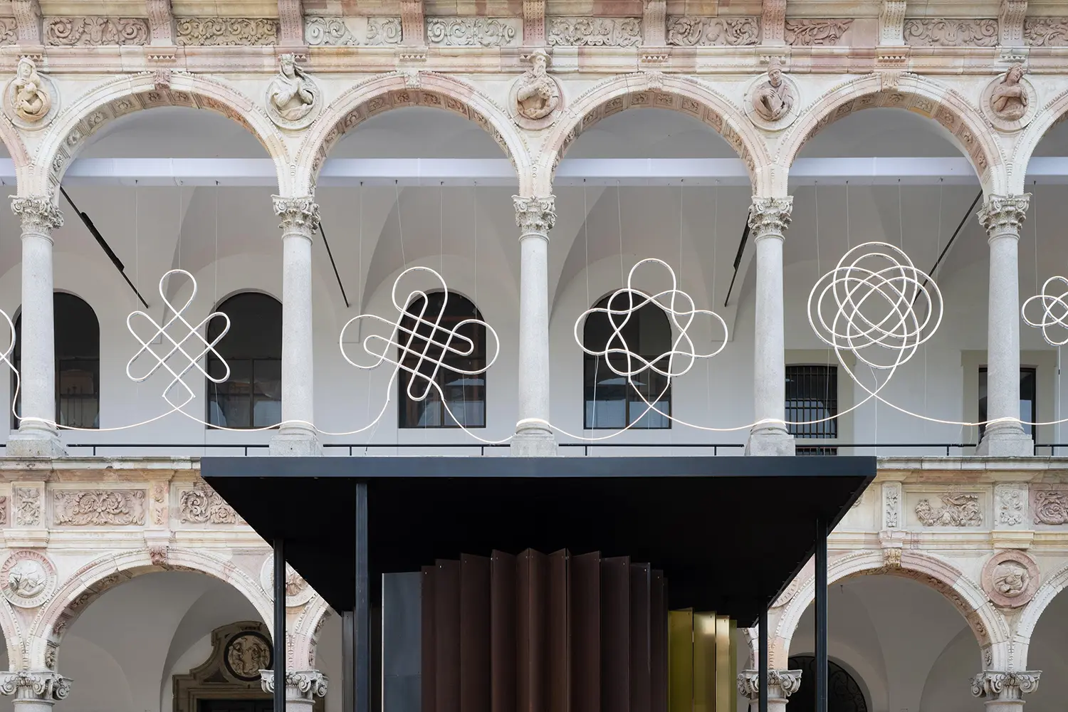 Symmetric view of four evolving LED knots suspended beneath the classical arches of the University of Milan.