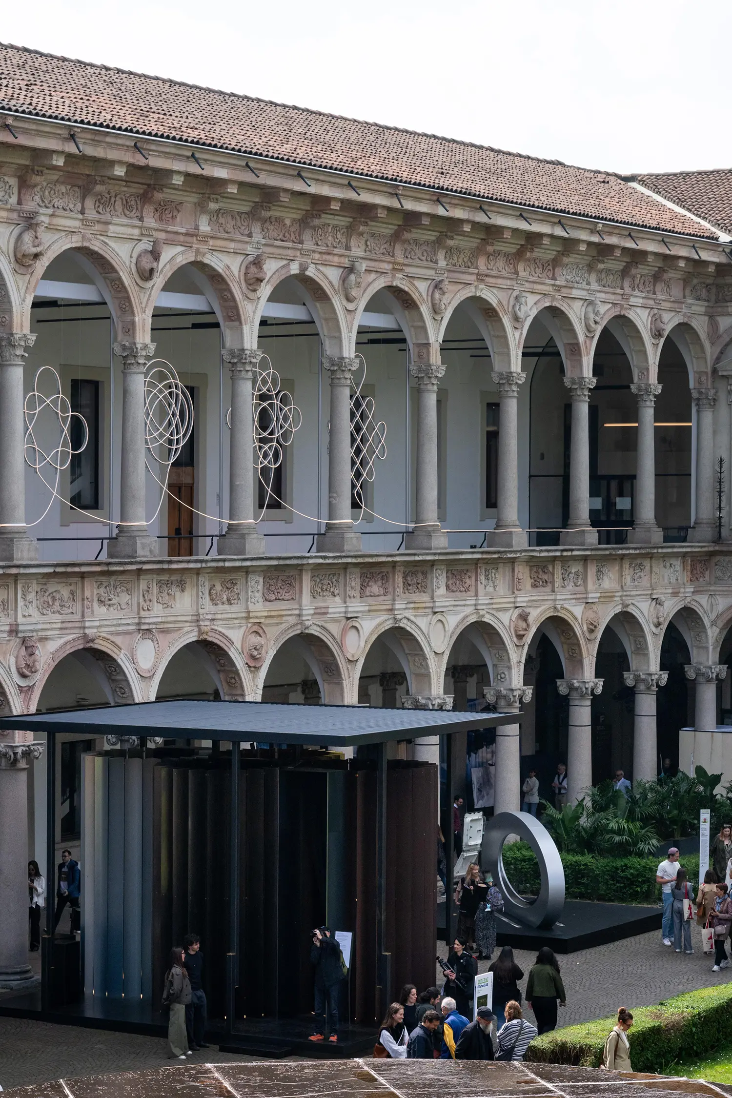 Wide angle of the Cortile d’Onore during Milan Design Week, featuring BIG’s light installation and other MateriAE works.