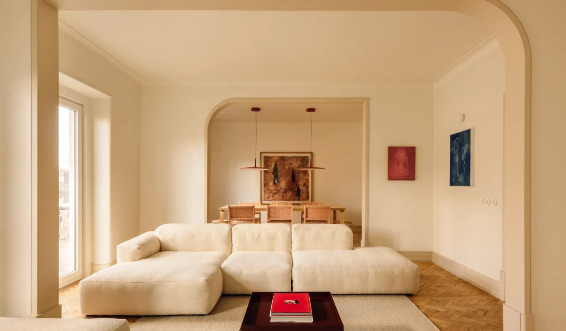 Minimalist living room in Lisbon with a modular white sofa, parquetry flooring, and arched doorways leading to a dining area.