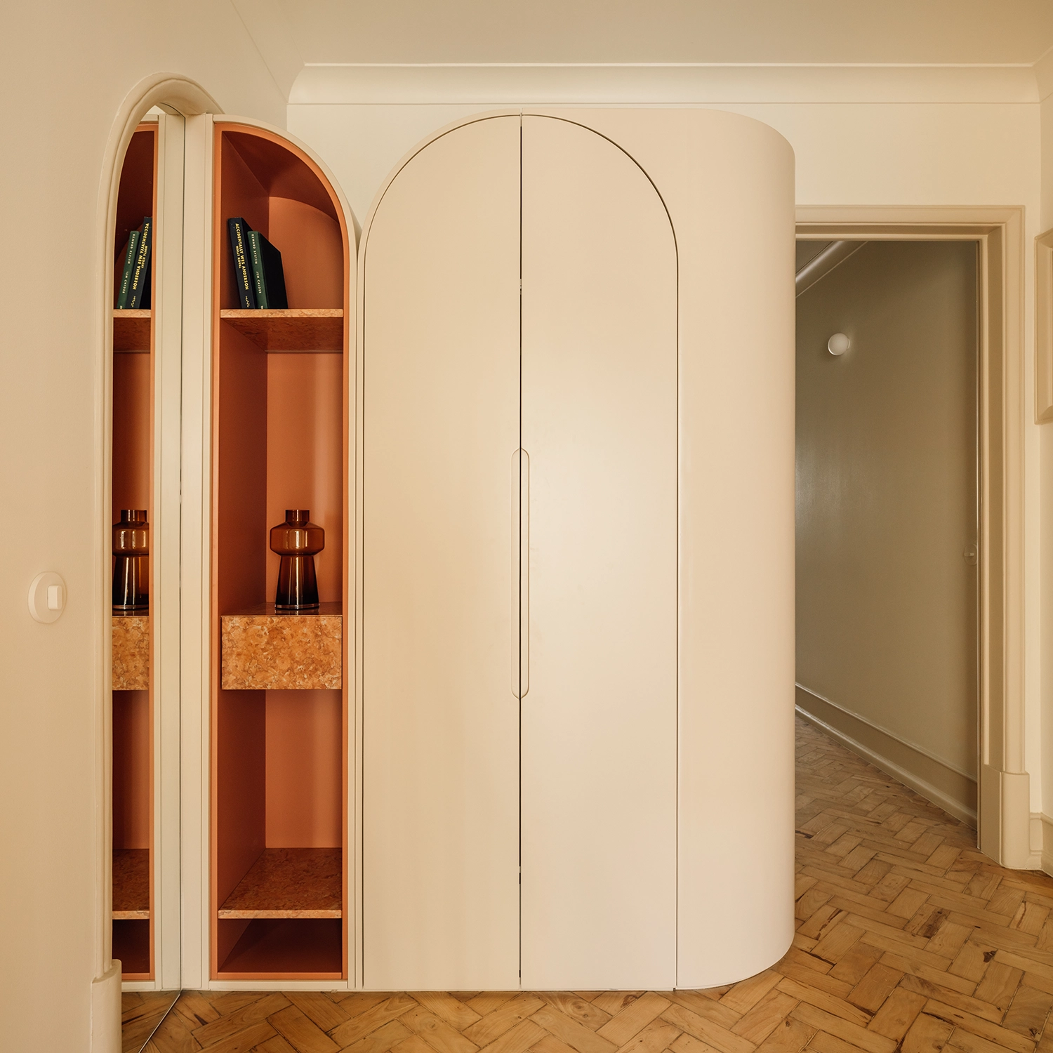 Curved cream-colored cabinetry with arched mirror and open shelving featuring terracotta-toned interior.