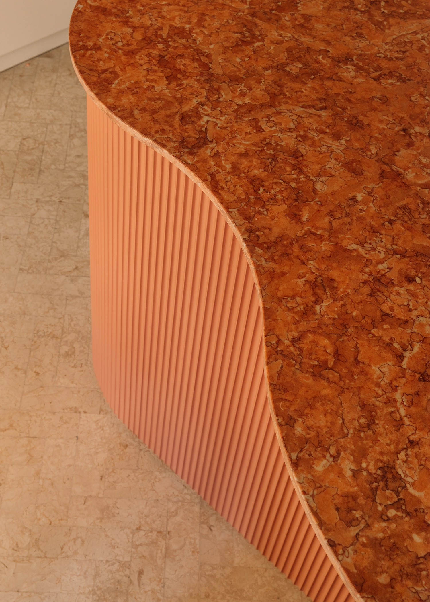 Close-up of a fluted terracotta kitchen island base topped with a speckled orange marble counter.