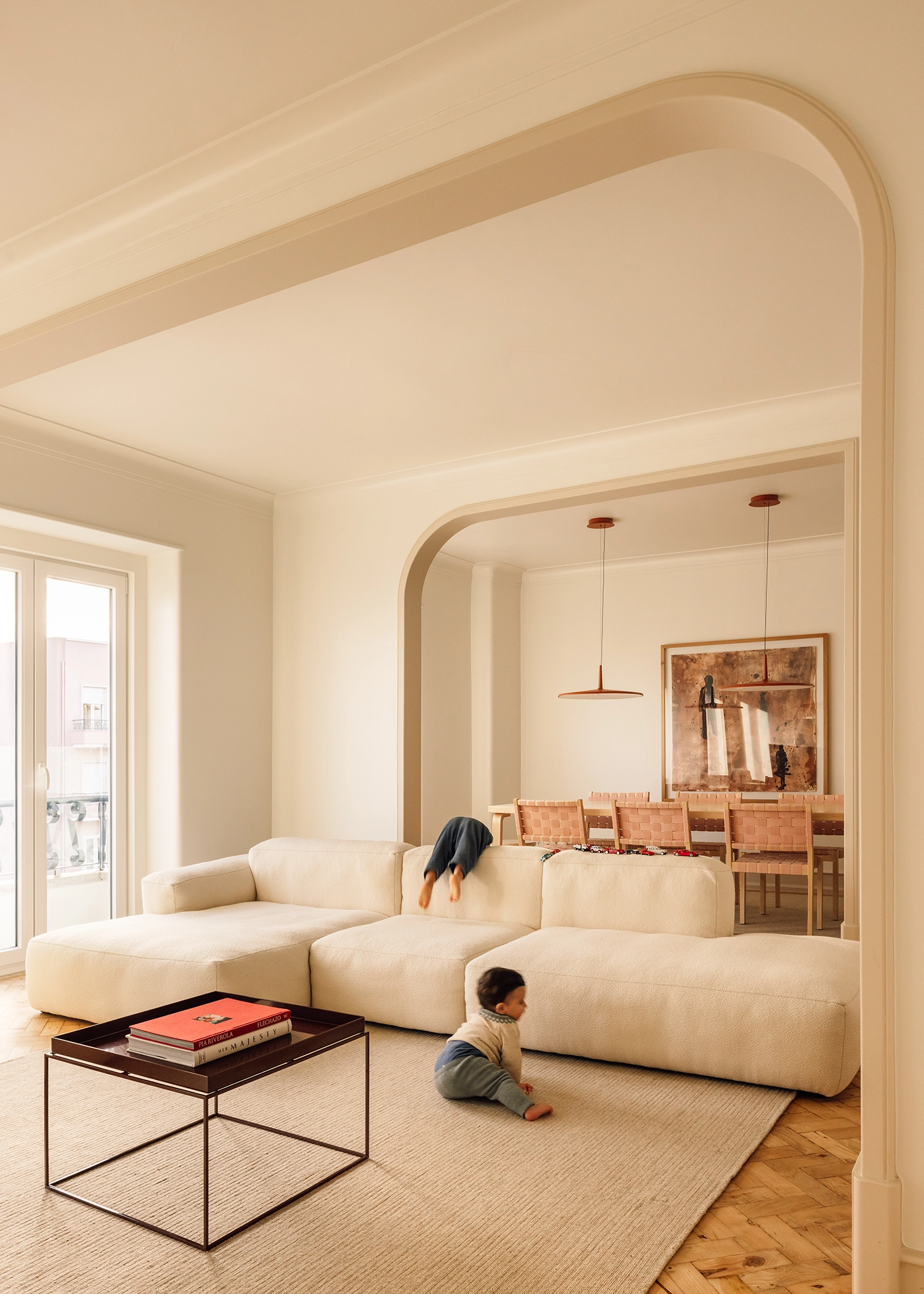 Living room scene with a child playing on a cream modular sofa framed by elegant arched wall openings.