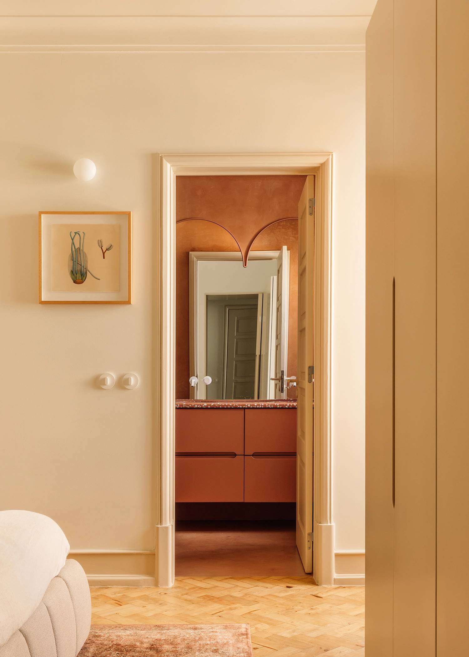 View through a doorway into a terracotta-toned bathroom with an arched mirror and integrated vanity.