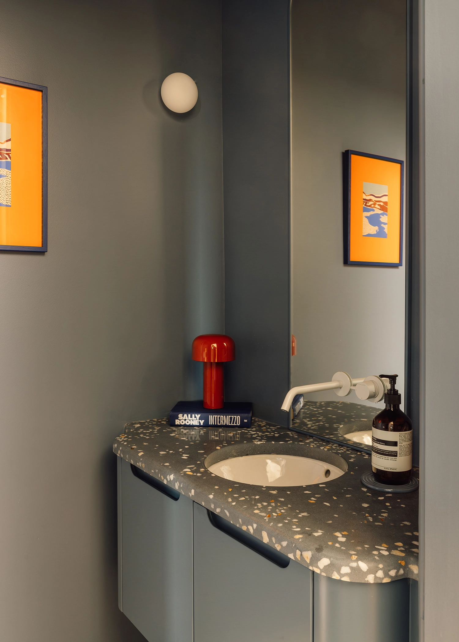 Dark grey bathroom with a speckled terrazzo countertop, integrated sink, and vibrant orange-framed artwork.