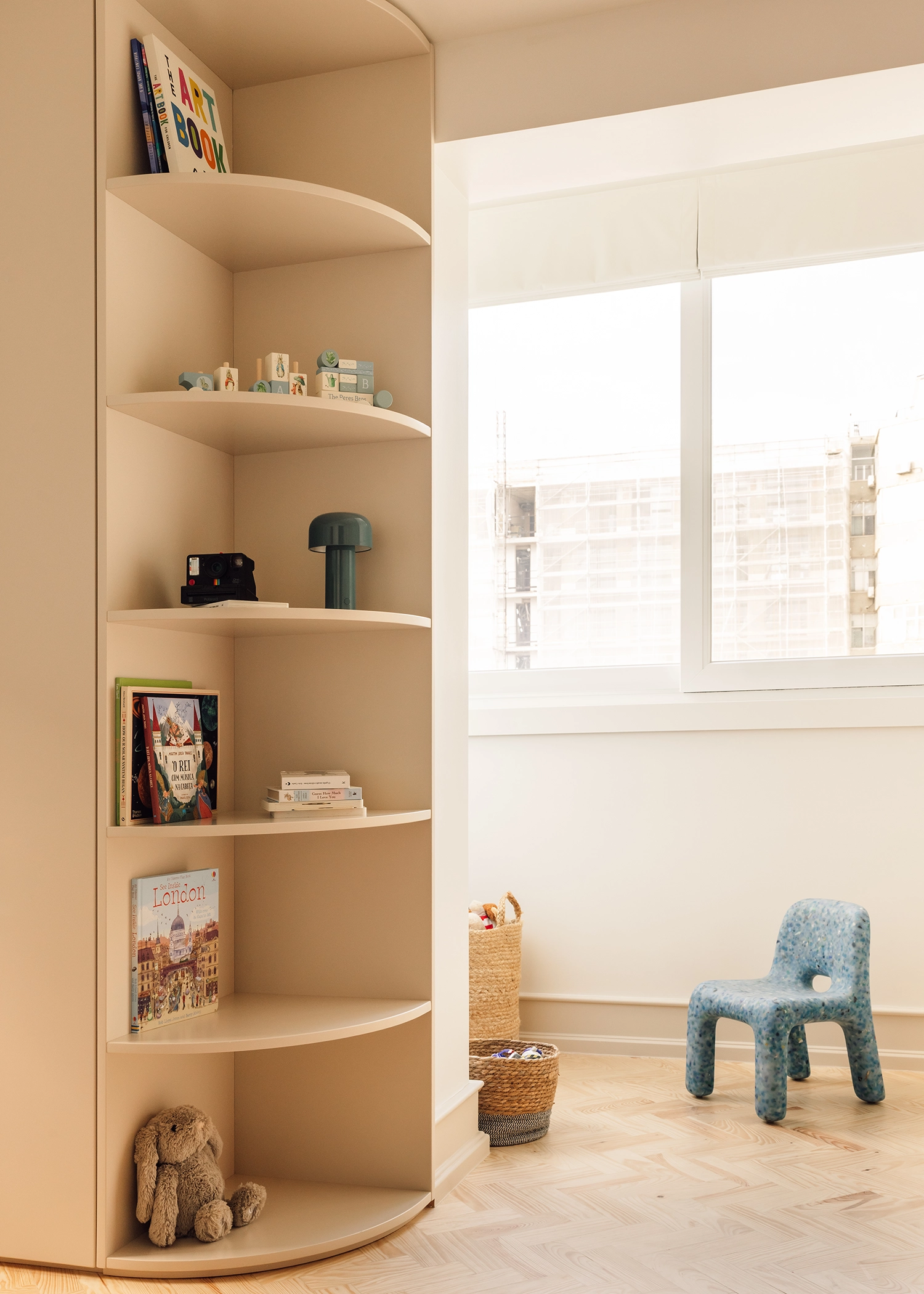 Built-in curved shelving unit in a bright nursery or playroom next to a large window.