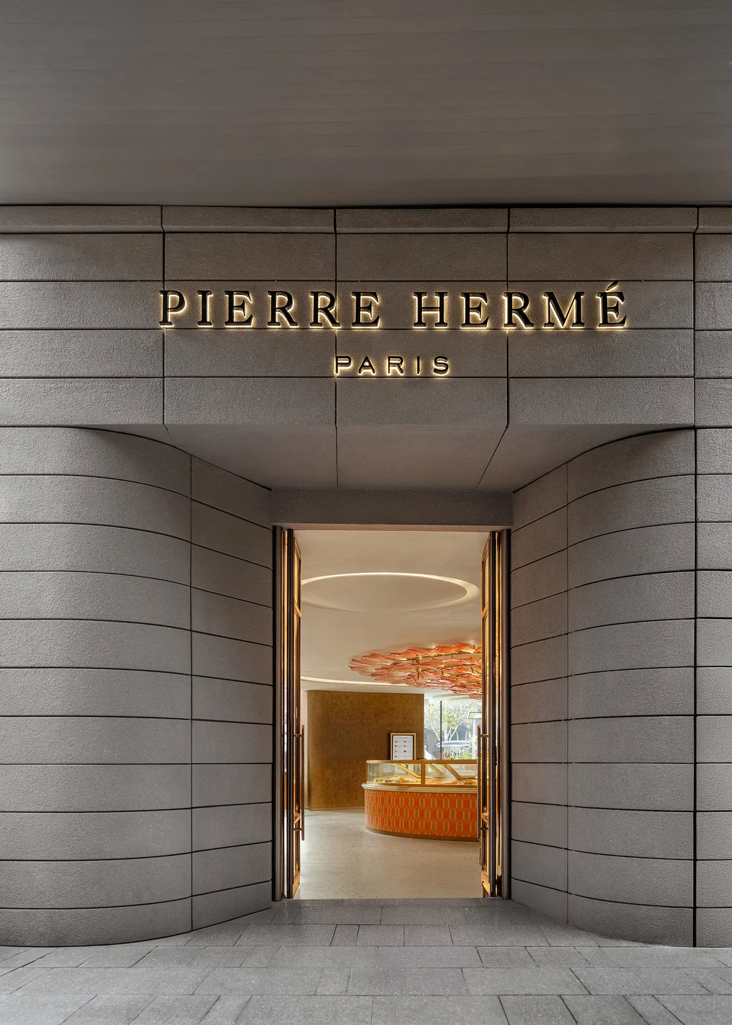 Exterior entrance of Pierre Hermé Paris in Singapore with grey stone walls and backlit signage.