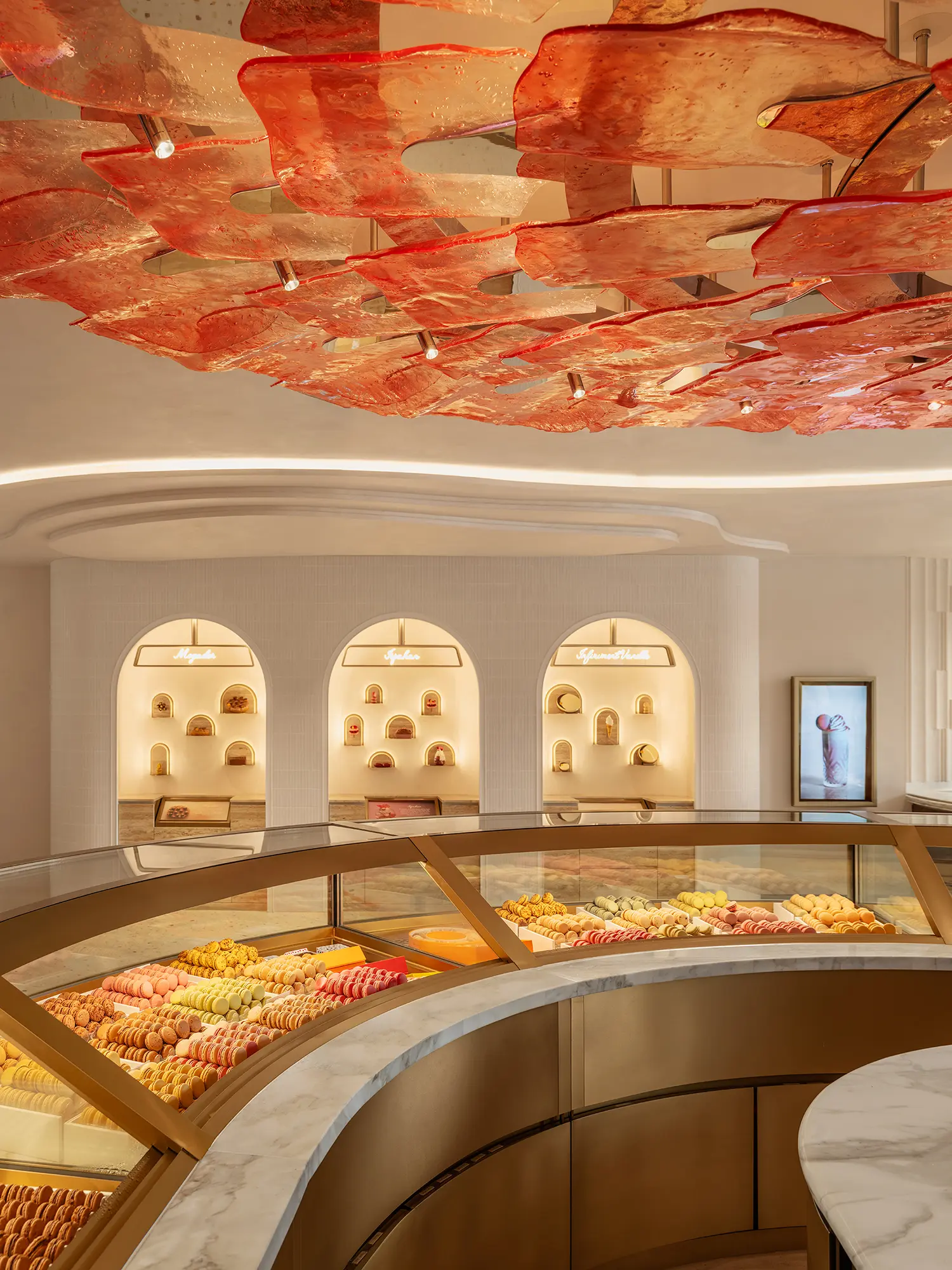 Detail of the curved glass display case filled with colorful macarons under a red glass ceiling.