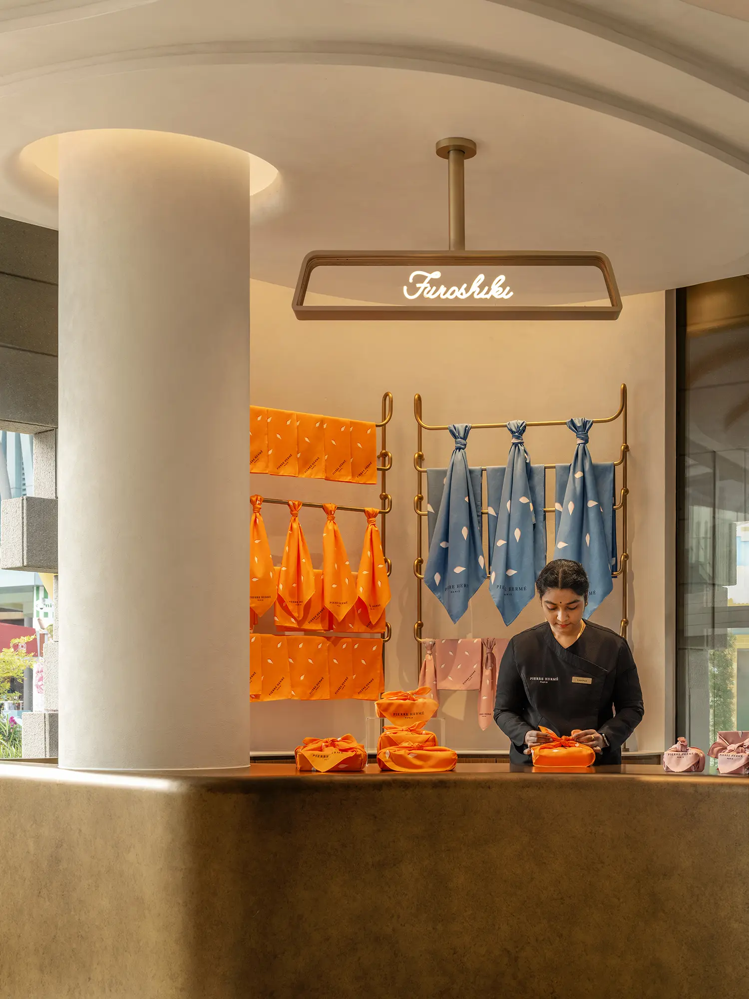 Staff member at the Furoshiki station wrapping gifts in orange and blue cloth.