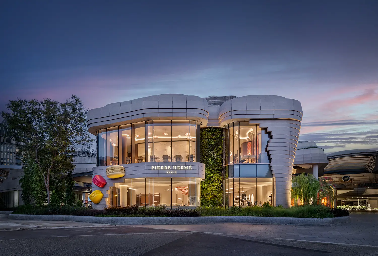 Night view of the Pierre Hermé Singapore building with curved white facades and large glass windows.