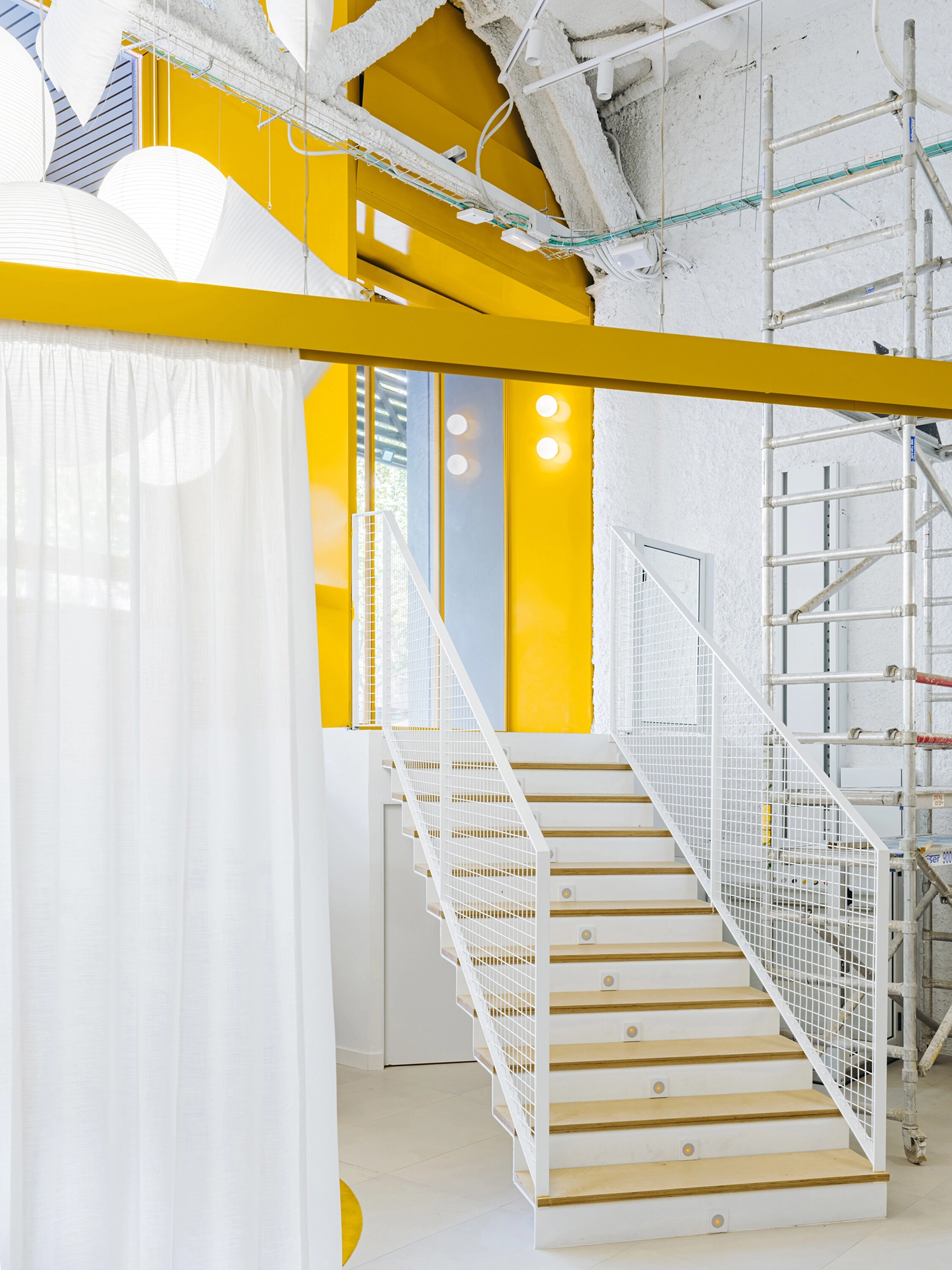 White staircase with yellow wall accents and industrial scaffolding in a retail space.