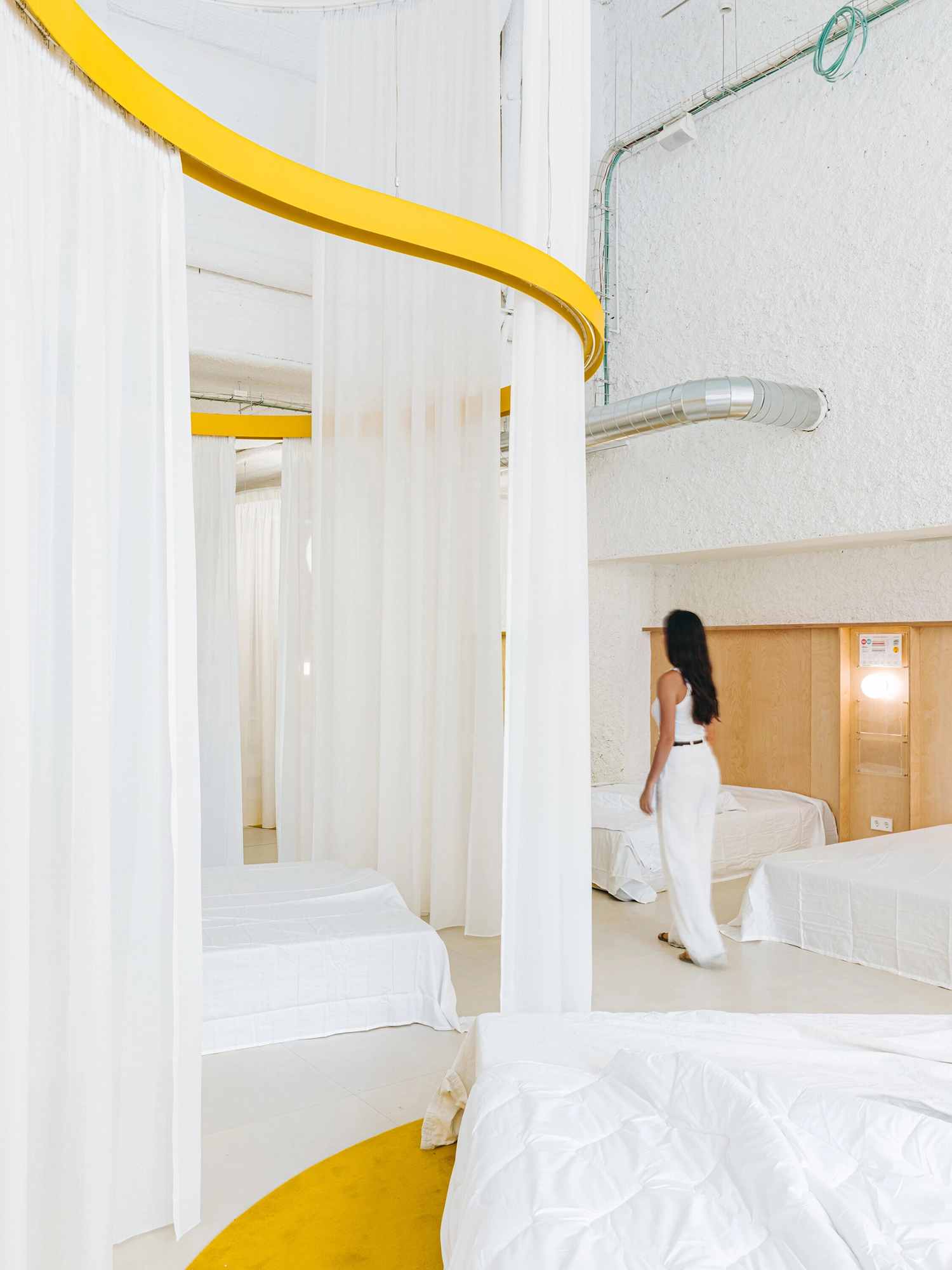 A woman walks through a mattress store designed with white curtains and yellow circular floor elements.