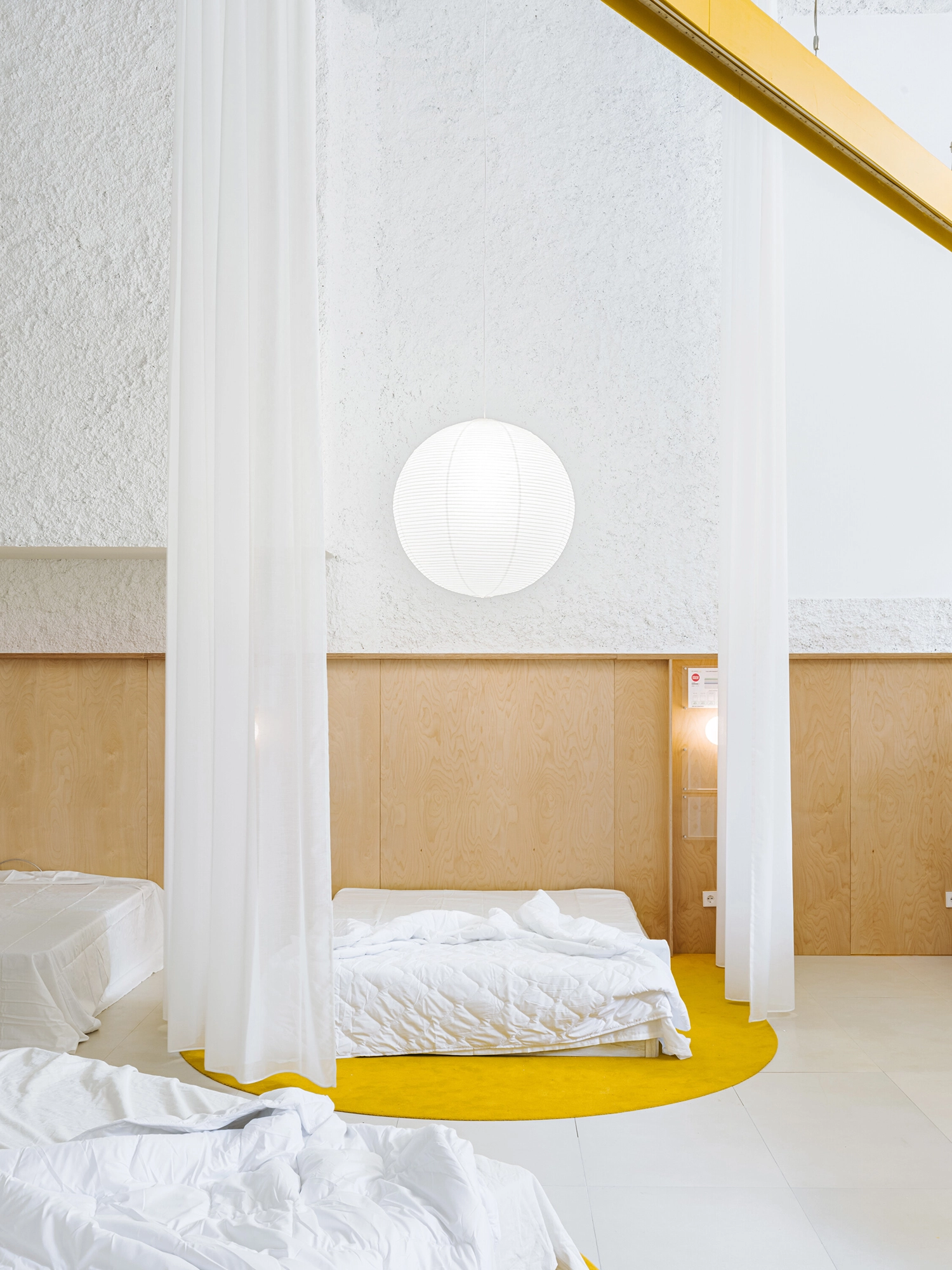Minimalist mattress display with a yellow circular rug and a large spherical paper lamp.