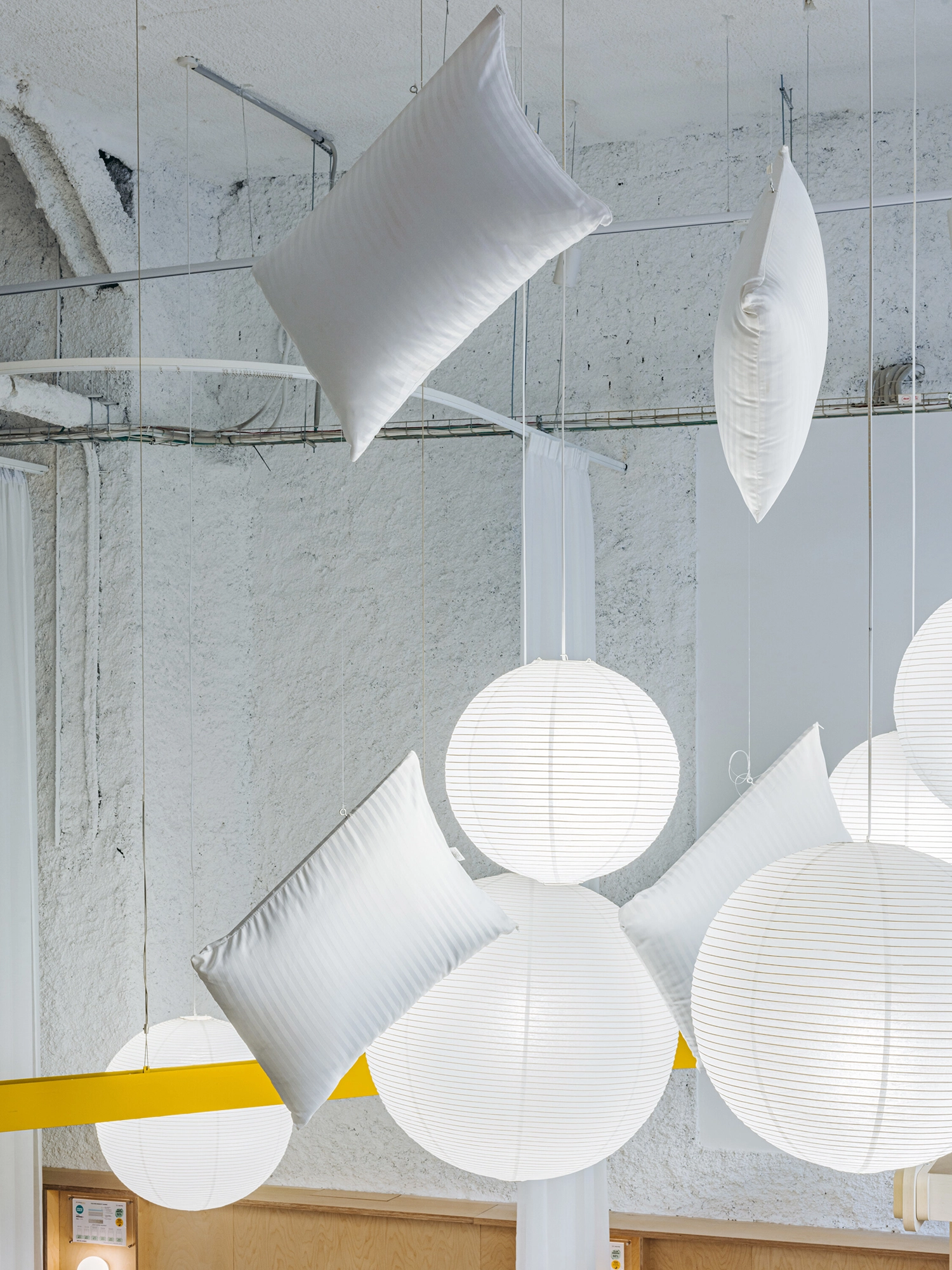 Suspended white pillows and spherical lamps hanging from a white textured ceiling.