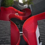 Aerial view of a winding red steel staircase between traditional Chinese grey tiled roofs in Nanjing.