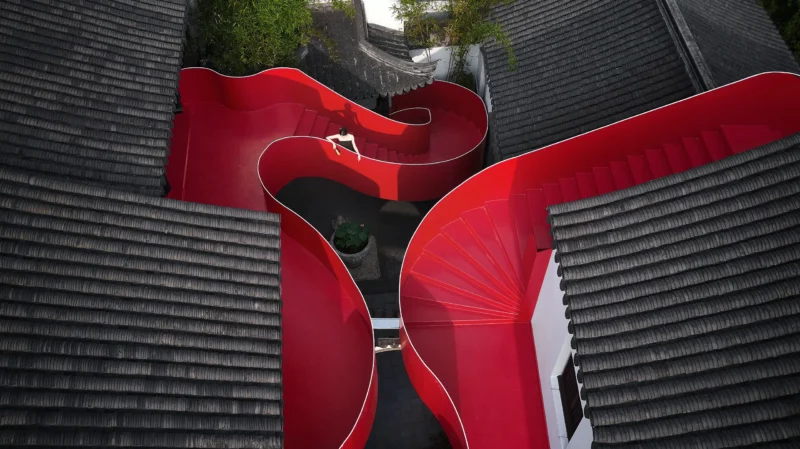Aerial view of a winding red steel staircase between traditional Chinese grey tiled roofs in Nanjing.
