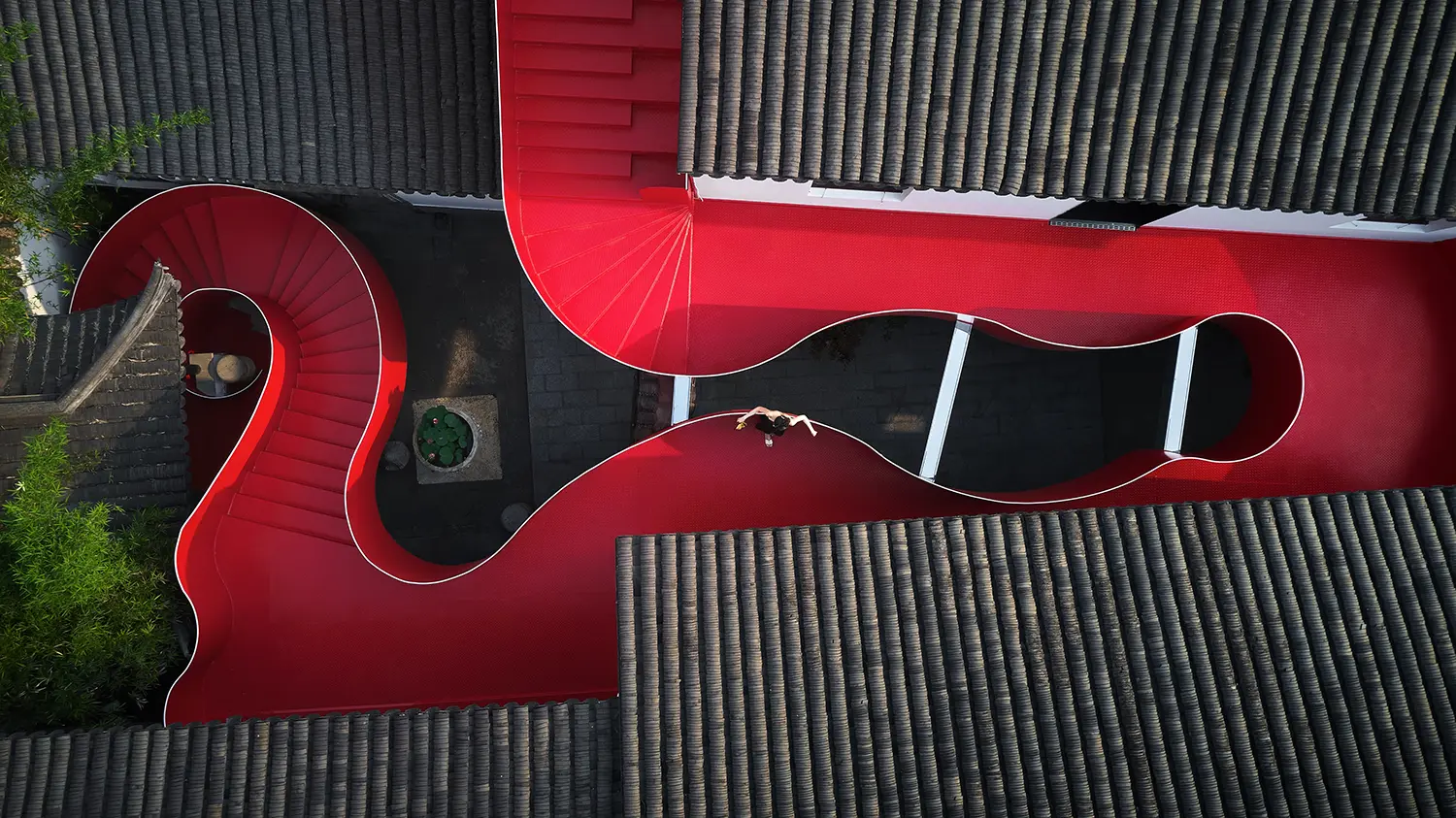Top-down view of a red serpentine walkway contrasting with dark grey roof tiles.