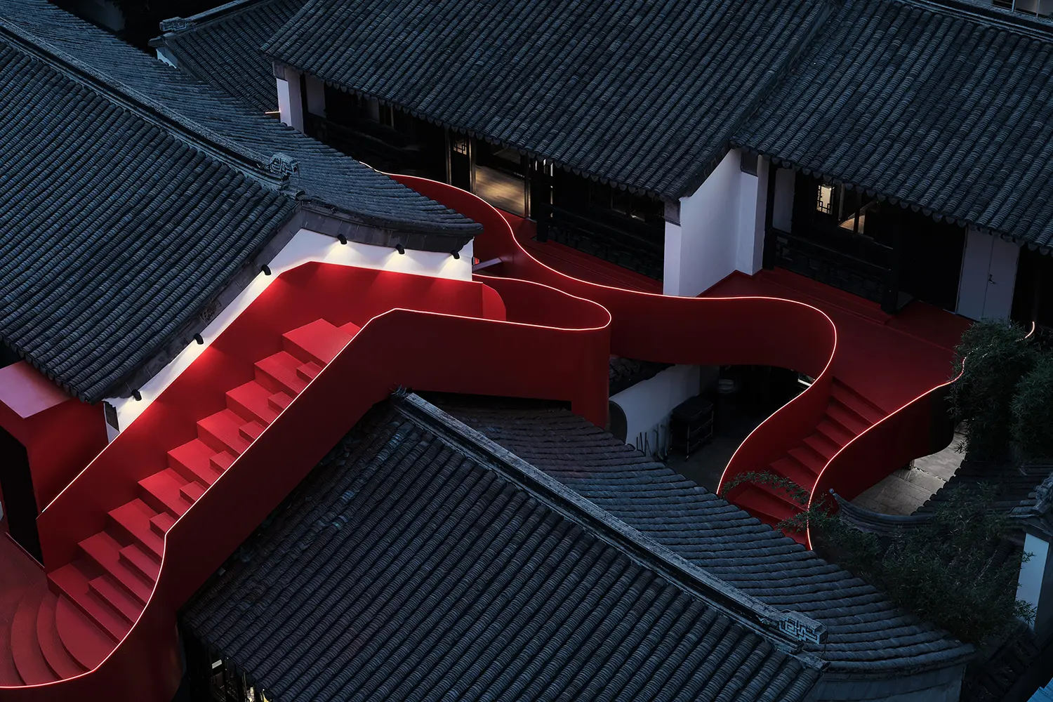 Night view of the illuminated red staircase weaving through dark traditional roofs in Nanjing.