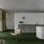 Brutalist concrete kitchen island and green carpet in a modern São Paulo interior.