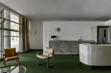 Brutalist concrete kitchen island and green carpet in a modern São Paulo interior.