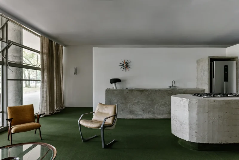 Brutalist concrete kitchen island and green carpet in a modern São Paulo interior.
