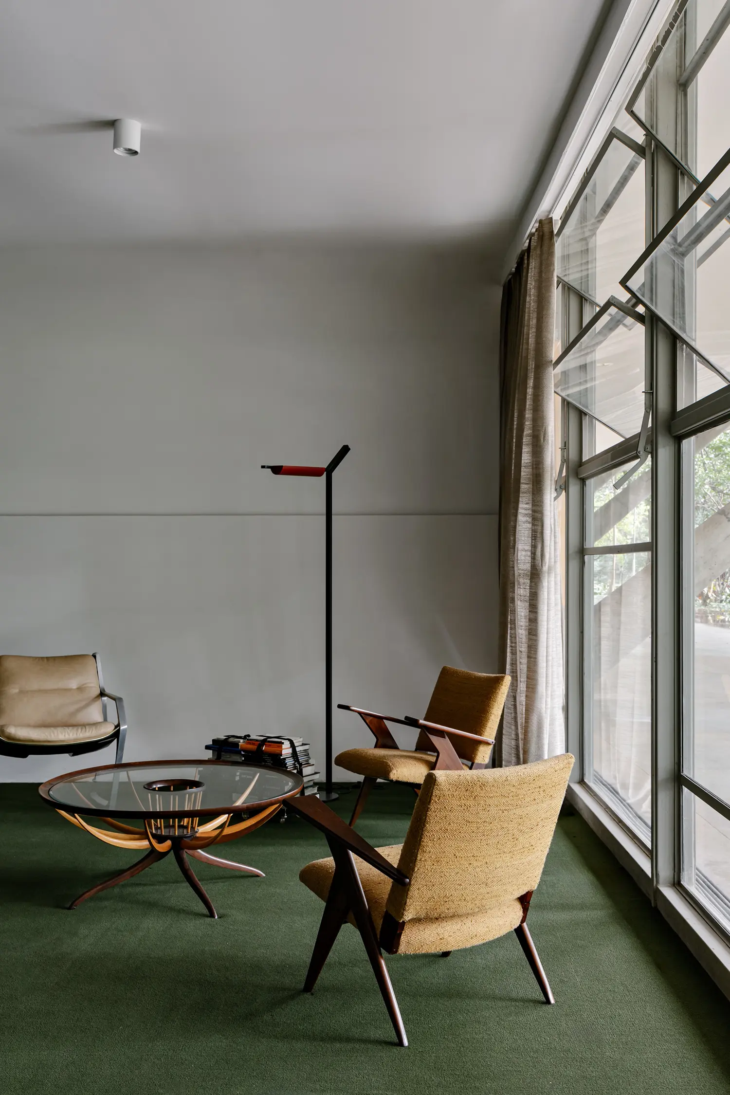 Mid-century modern wooden armchairs and glass coffee table on green carpet.