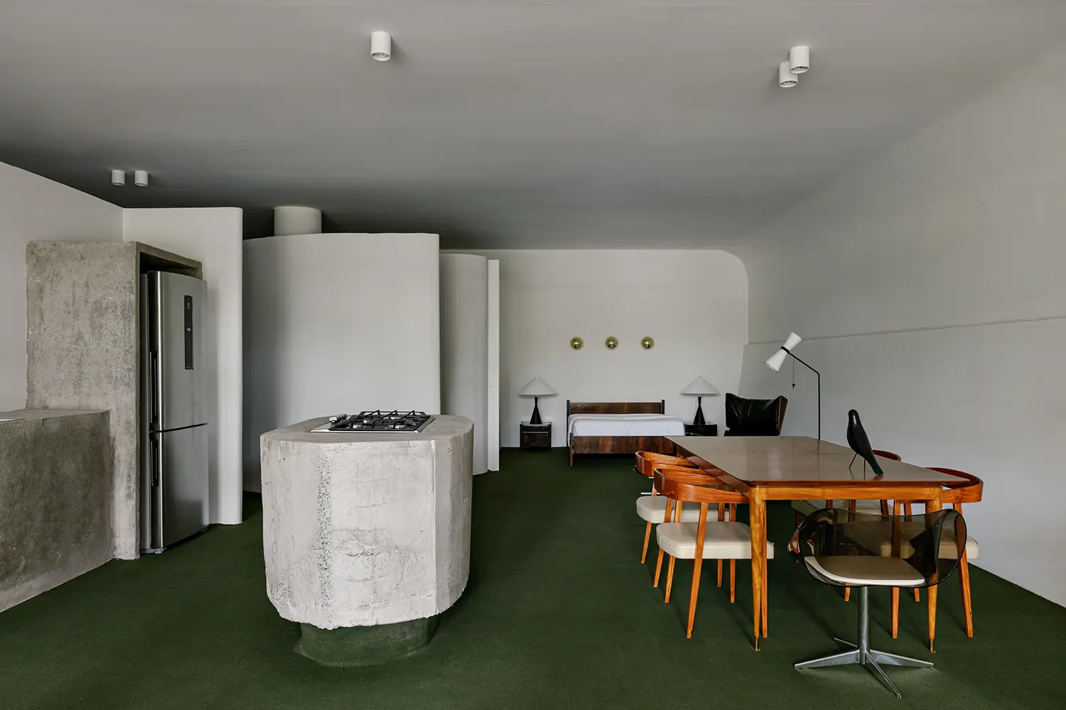 Minimalist bedroom and dining area separated by curved white partitions.