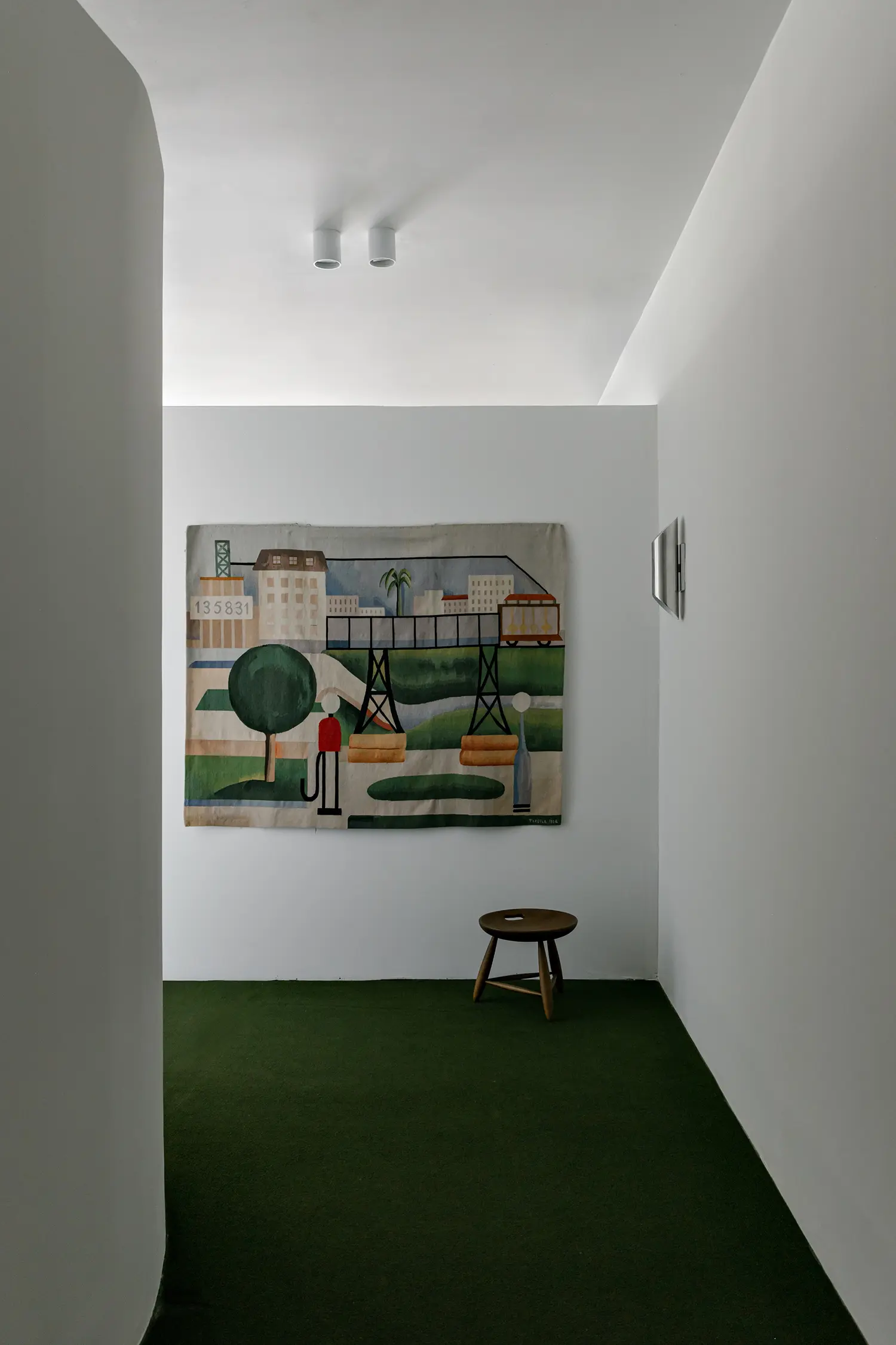 Tarsila do Amaral tapestry hanging in a minimalist white corridor with green carpet.