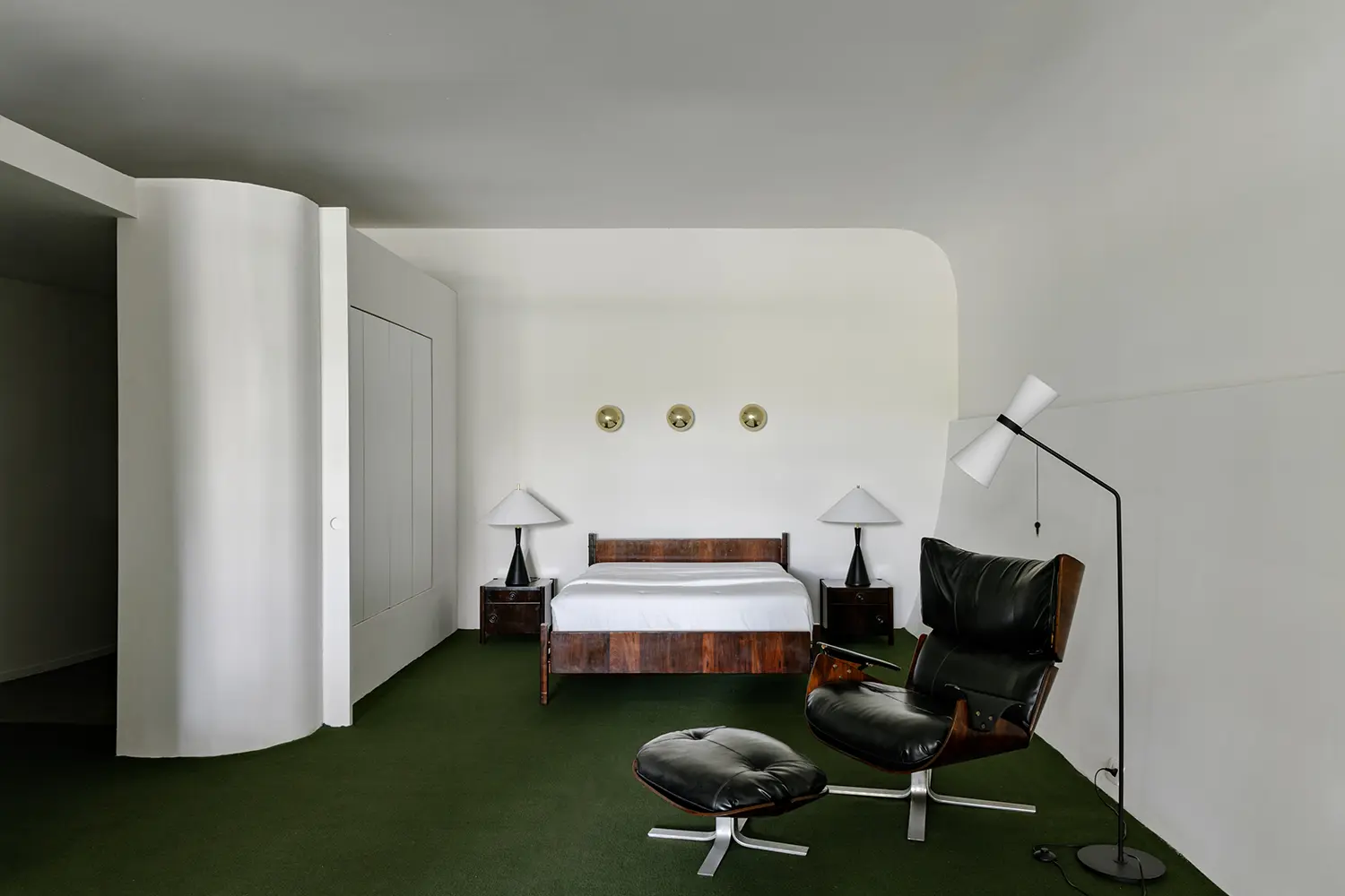 Modernist wood bed frame and Eames Lounge Chair in a white minimalist bedroom.