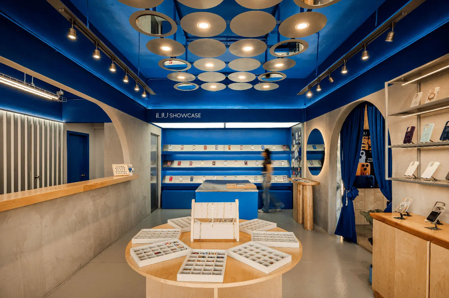 Wide shot of iLIU Experience retail interior showing circular ceiling luminaires and wooden display tables.