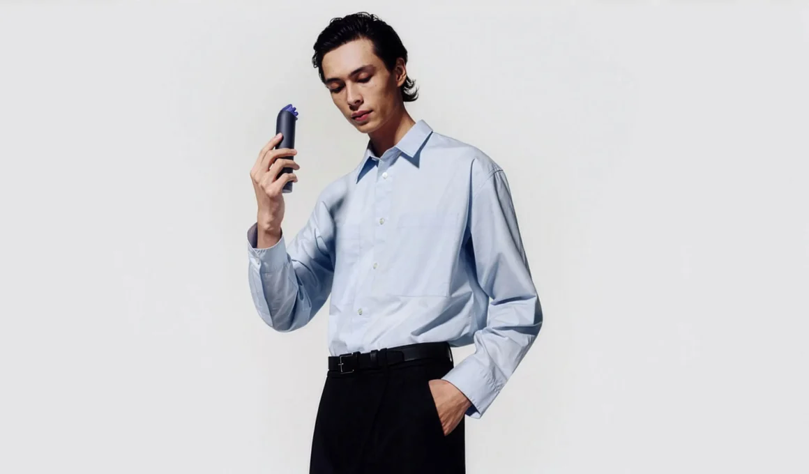A person holding a navy blue Dyson HushJet Mini Cool portable fan against a white background.