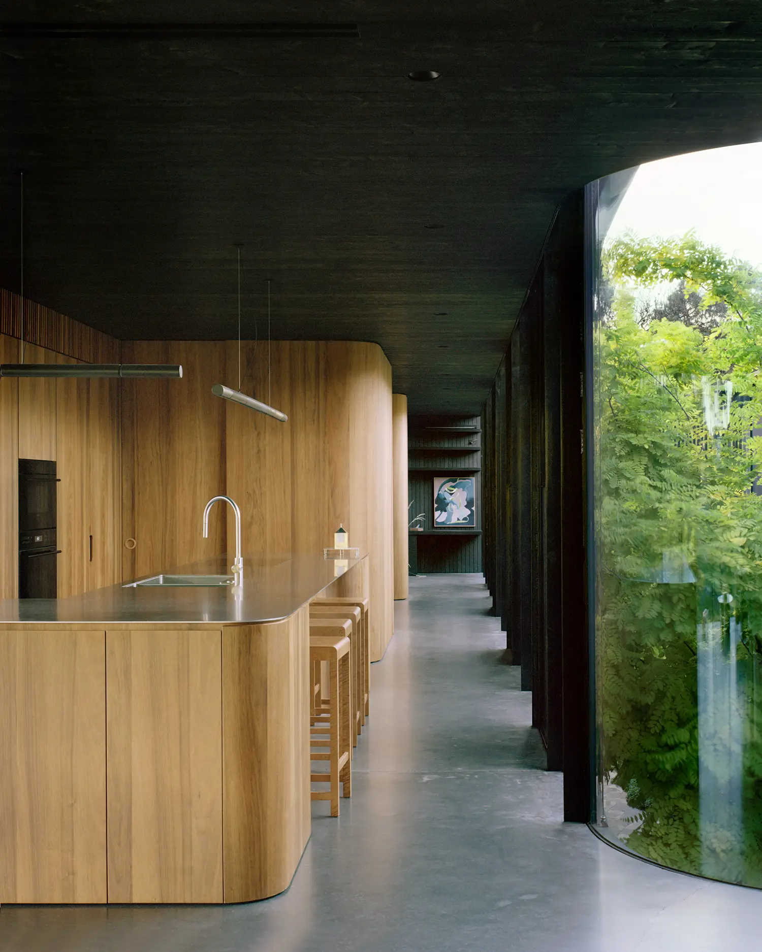 Interior of a modern kitchen featuring a long stainless steel island and curved timber walls.