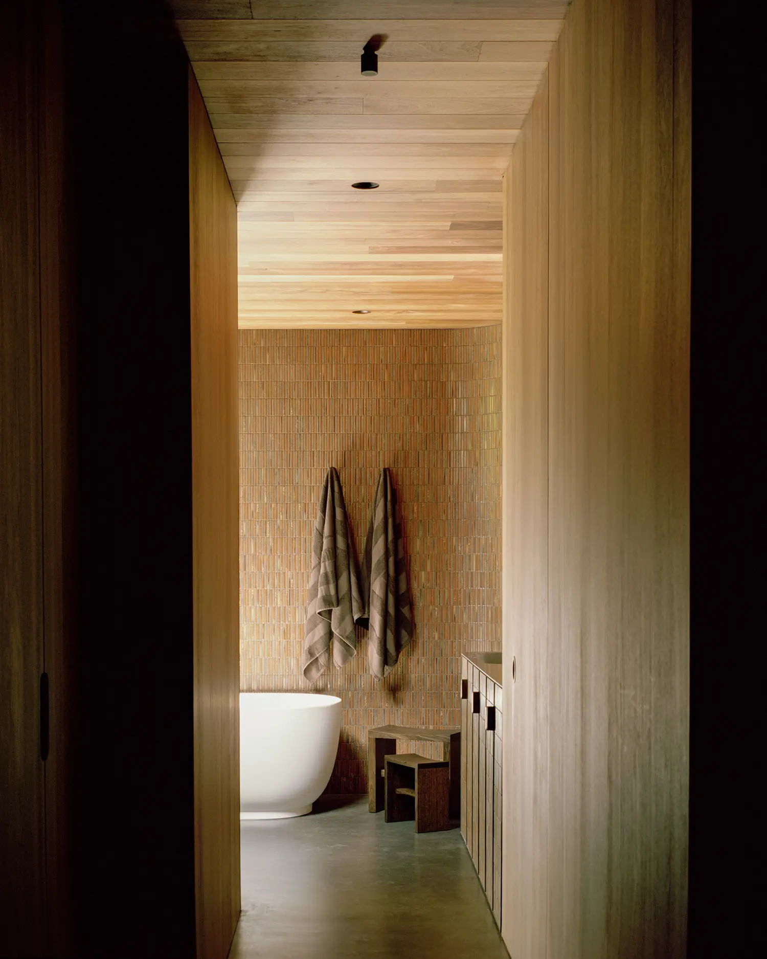Minimalist bathroom featuring a white freestanding bathtub and vertical mosaic tiles.
