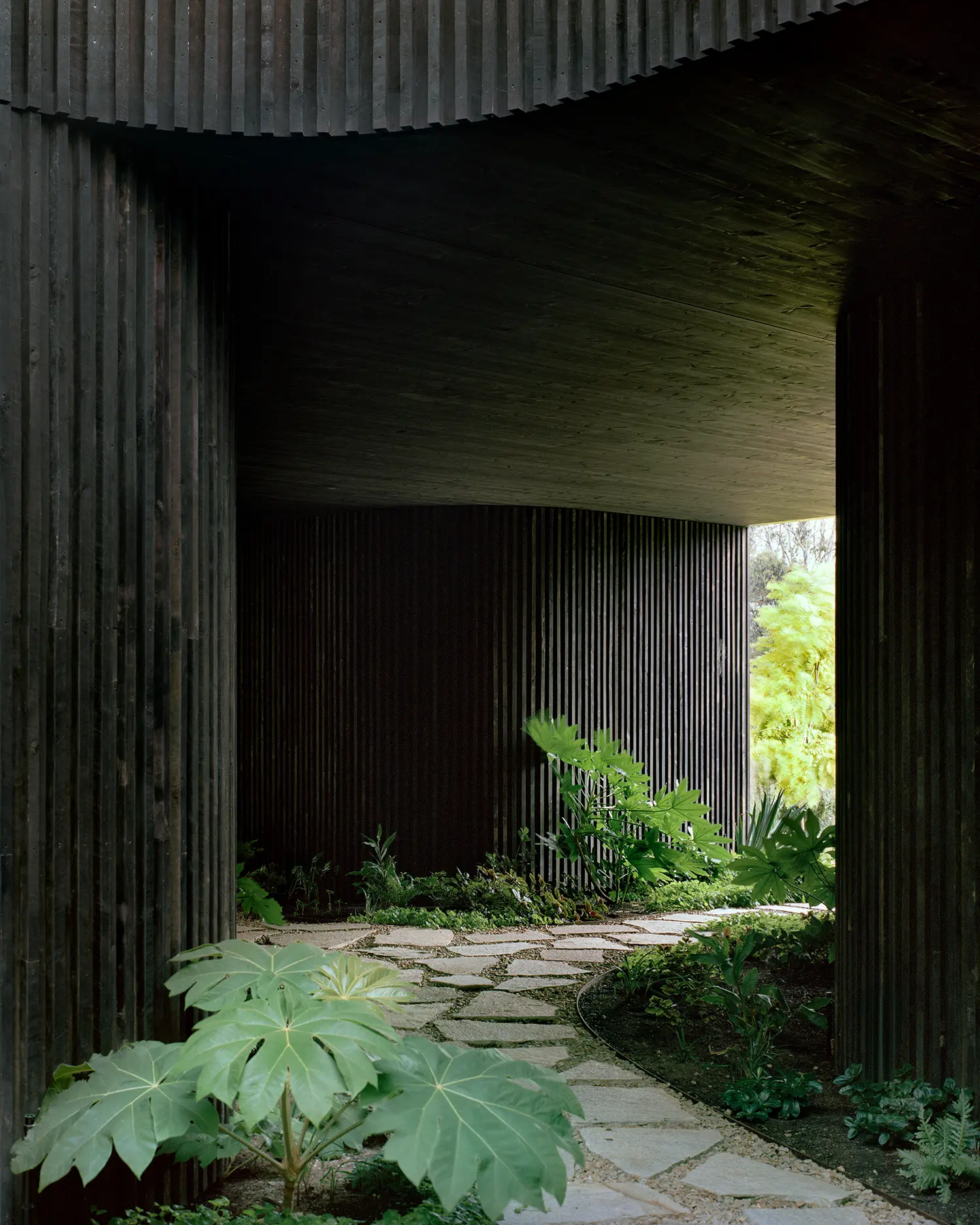 Close-up of the dark vertical timber batten walls and stone paving at the lower ground level.