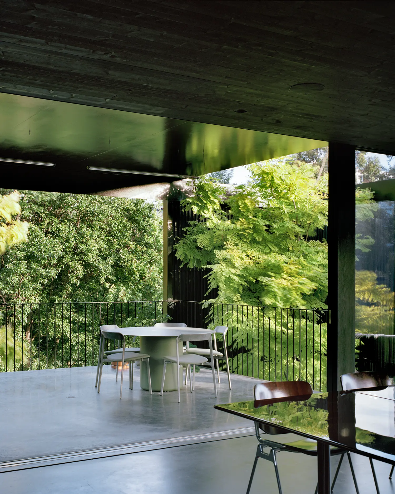 An outdoor dining terrace with a round table and grey chairs, overlooking dense trees.