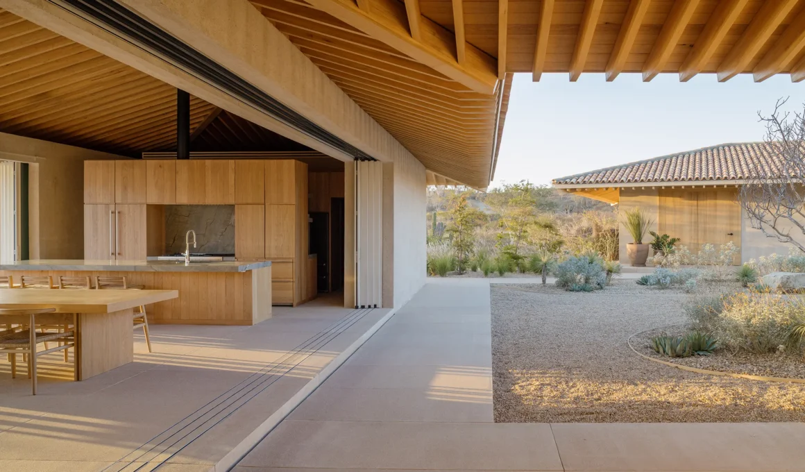 Open-plan kitchen and dining area with wooden cabinetry and exposed oak roof beams opening to a gravel courtyard.