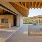 Open-plan kitchen and dining area with wooden cabinetry and exposed oak roof beams opening to a gravel courtyard.