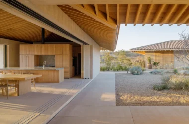 Open-plan kitchen and dining area with wooden cabinetry and exposed oak roof beams opening to a gravel courtyard.