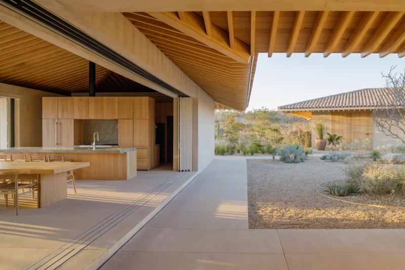 Open-plan kitchen and dining area with wooden cabinetry and exposed oak roof beams opening to a gravel courtyard.
