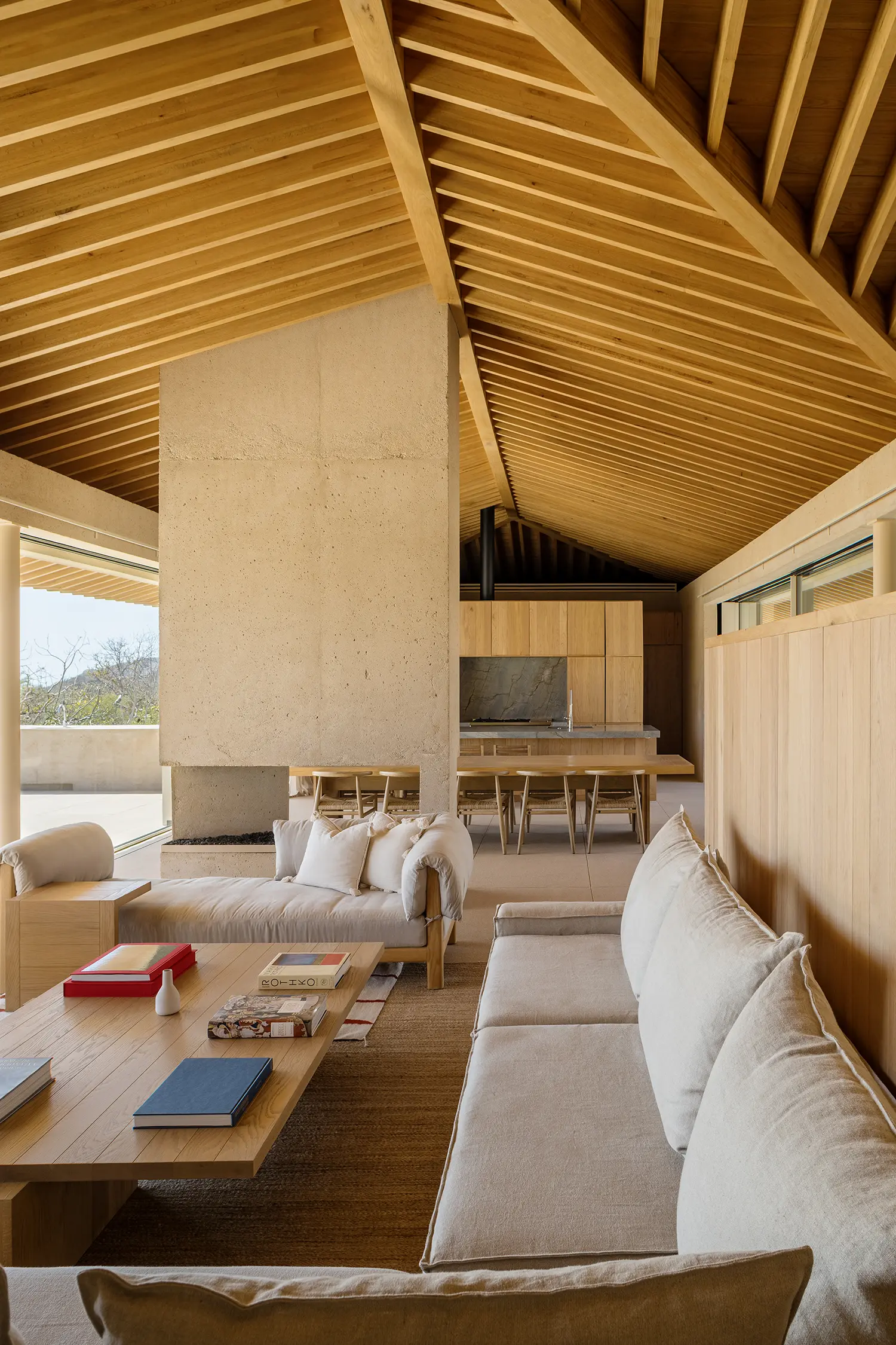 Living room with a neutral sofa and large concrete fireplace under a high-pitched wooden ceiling.